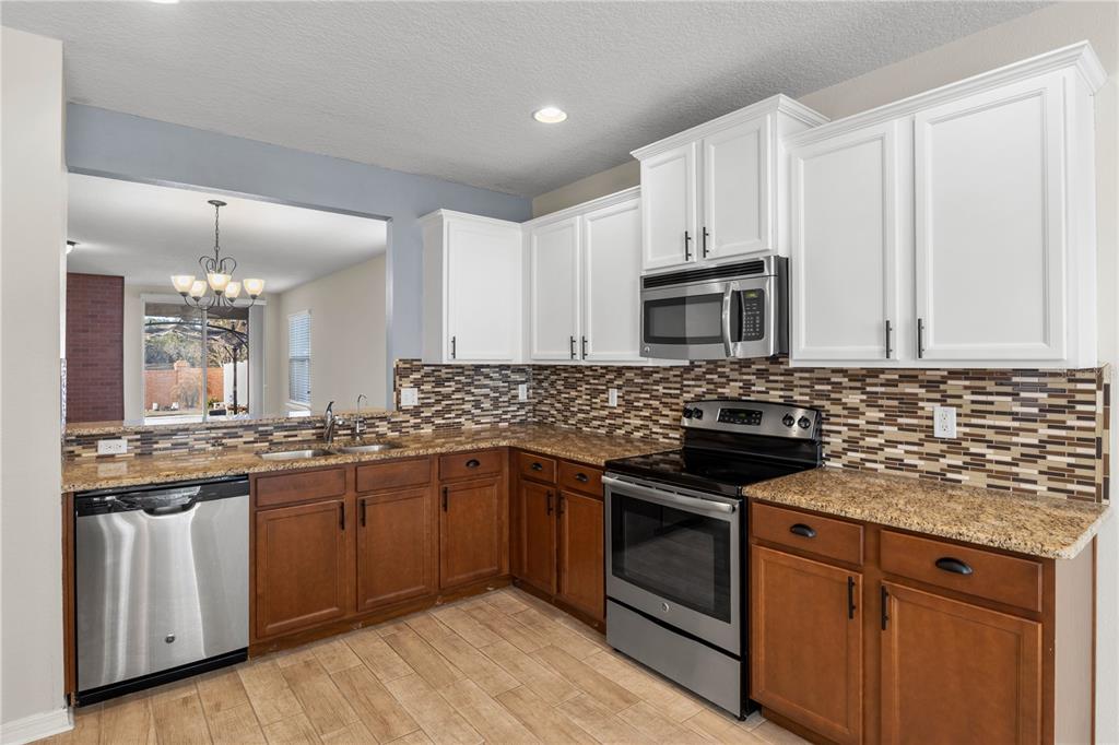 A kitchen features two-tone cabinets, granite countertops, stainless steel appliances, and a mosaic tile backsplash — 8017 PAGE COURT, HAINES CITY, FL