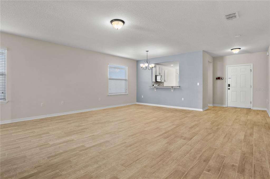 An open-concept living room features light wood-look tile flooring, neutral walls, and a kitchen pass-through — 8017 PAGE COURT, HAINES CITY, FL