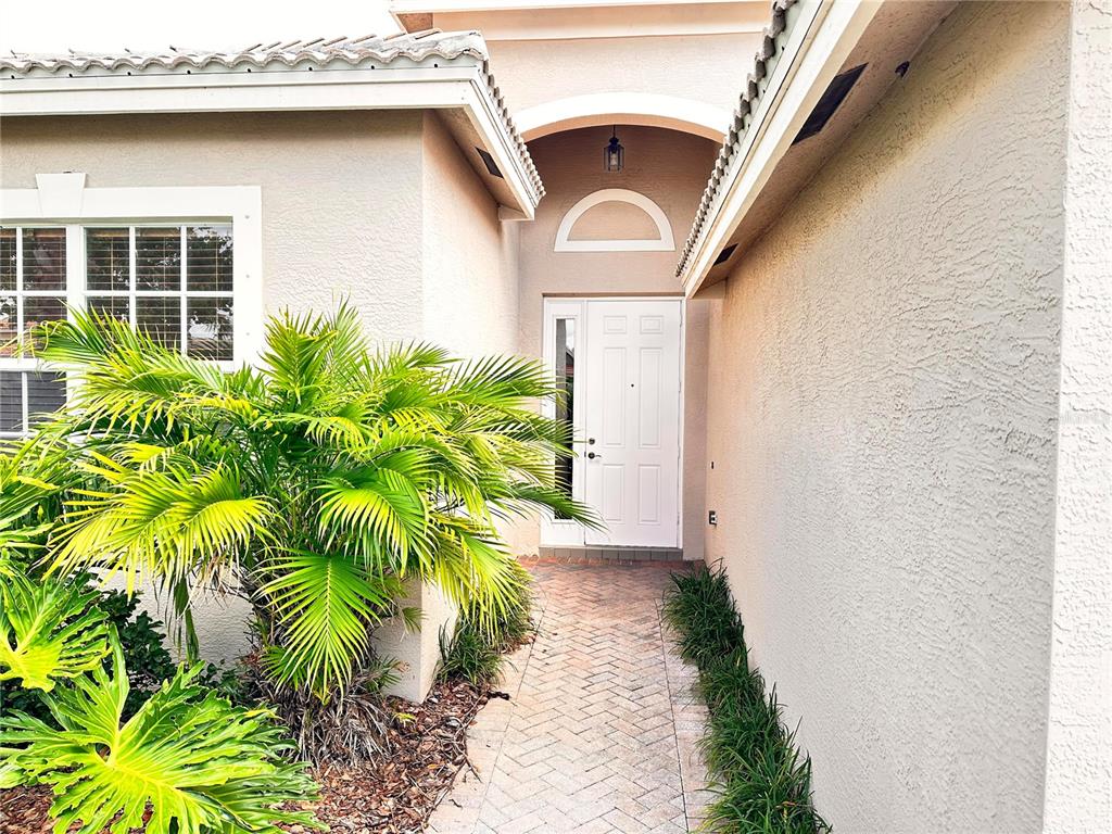 A paved walkway leads to a white front door under a recessed arched entryway — 4950 SANDY BROOK CIRCLE, WIMAUMA, FL