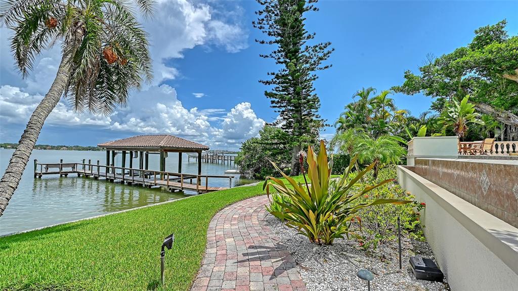 A brick walkway leads toward a wooden boat dock on a waterfront property with palms — 1216 N CASEY KEY ROAD, OSPREY, FL
