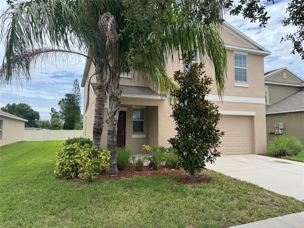 A two-story tan stucco house with a palm tree, front porch, and attached garage — 405 SERENITY MILL LOOP, RUSKIN, FL