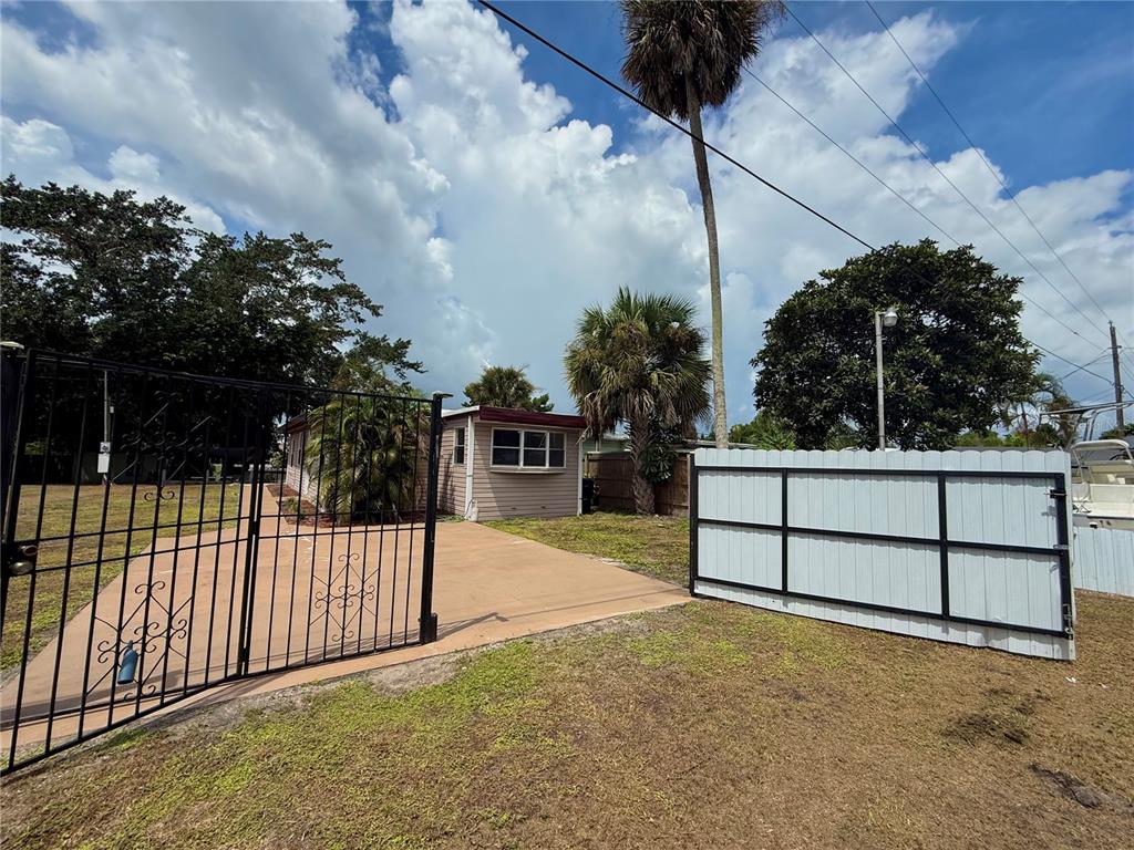 A paved driveway leads to a small house behind a black metal gate and fence — 3603 SE 35TH AVENUE, OKEECHOBEE, FL