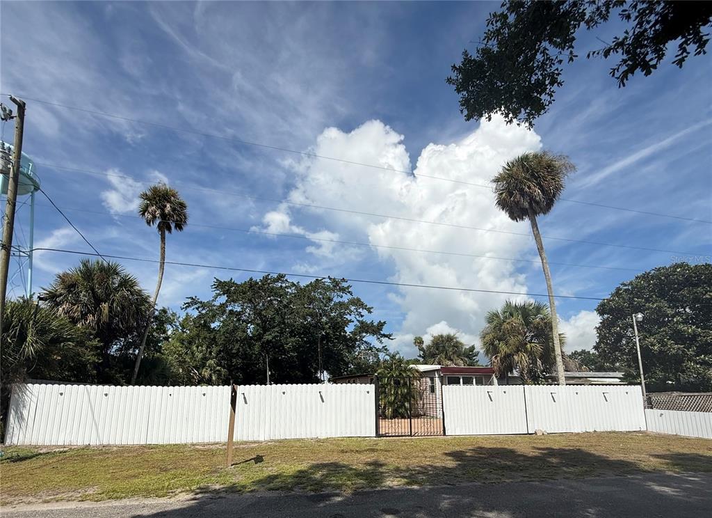 A white fence encloses a property with palm trees and a house under a cloudy sky — 3603 SE 35TH AVENUE, OKEECHOBEE, FL