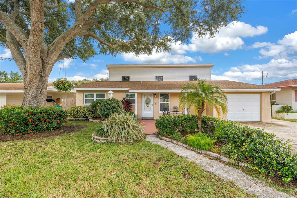 A single-story house with a tan exterior, a white garage door, and a large oak tree — 7999 RIDGE ROAD, SEMINOLE, FL