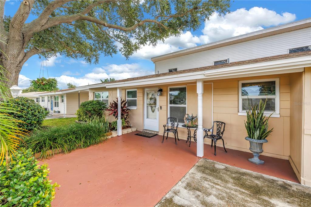 A covered patio with a red concrete floor sits in front of a tan house — 7999 RIDGE ROAD, SEMINOLE, FL
