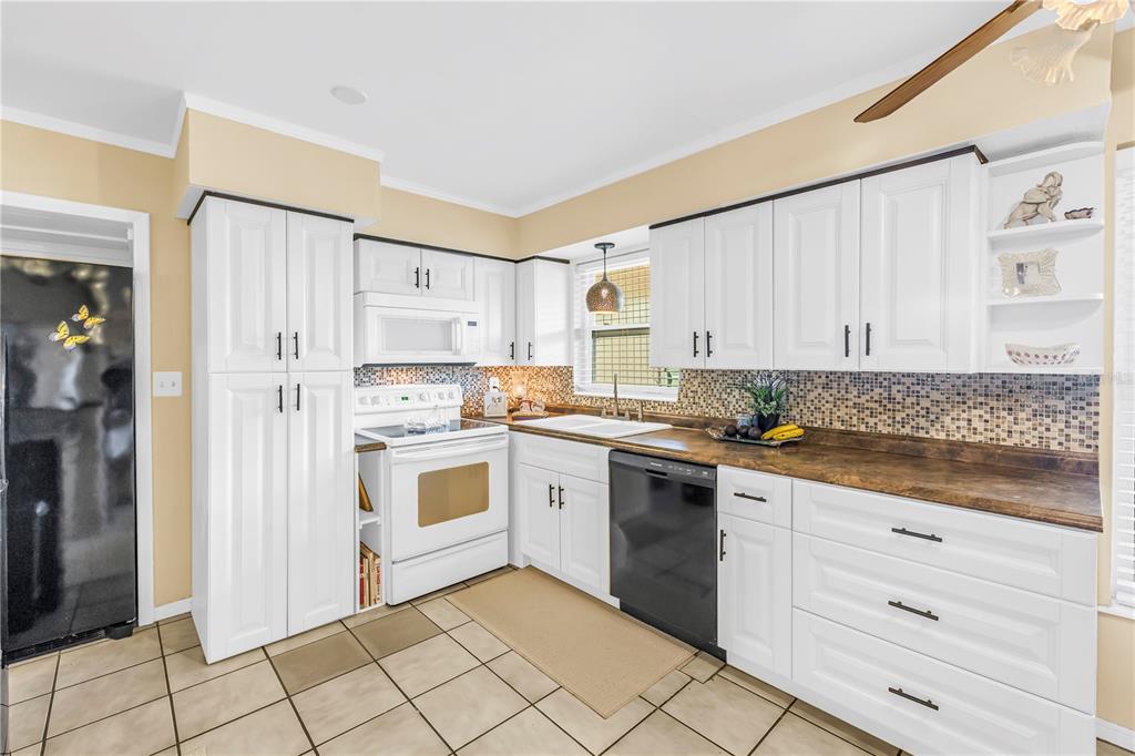A kitchen features white cabinets, a dark countertop, a tiled backsplash, and a black dishwasher — 7999 RIDGE ROAD, SEMINOLE, FL