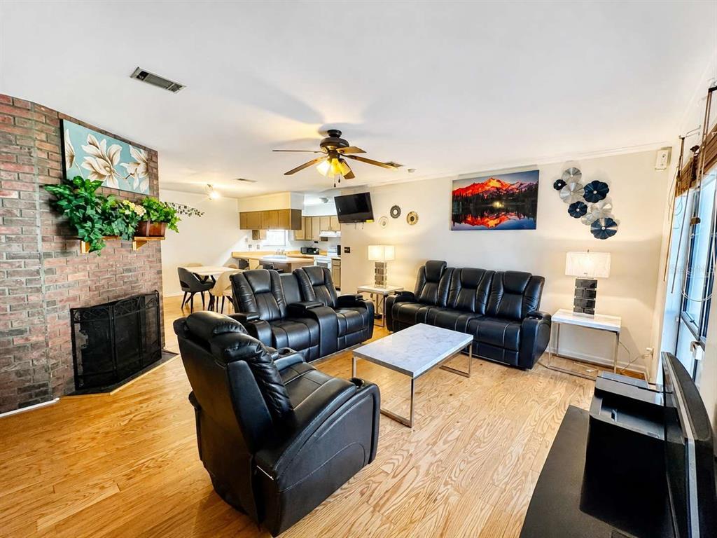 A living room with a brick fireplace, black leather furniture, and light wood flooring — 6018 NW 26TH TERRACE, GAINESVILLE, FL