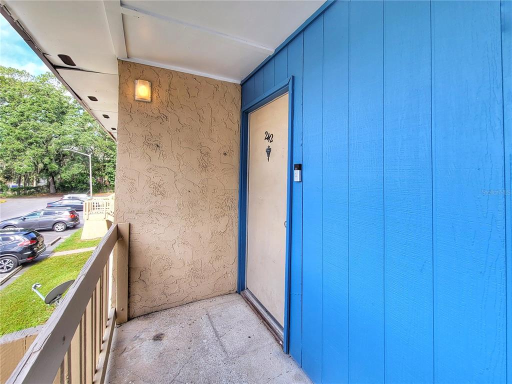 An exterior view of a balcony with a beige door numbered 242 and blue siding — 2811 SW ARCHER ROAD UNIT Z242, GAINESVILLE, FL
