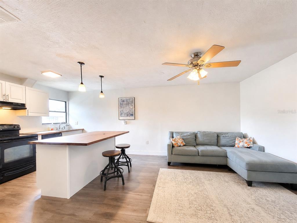 An open-concept kitchen and living area features a wooden island, bar stools, and a sectional sofa — 2811 SW ARCHER ROAD UNIT Z242, GAINESVILLE, FL