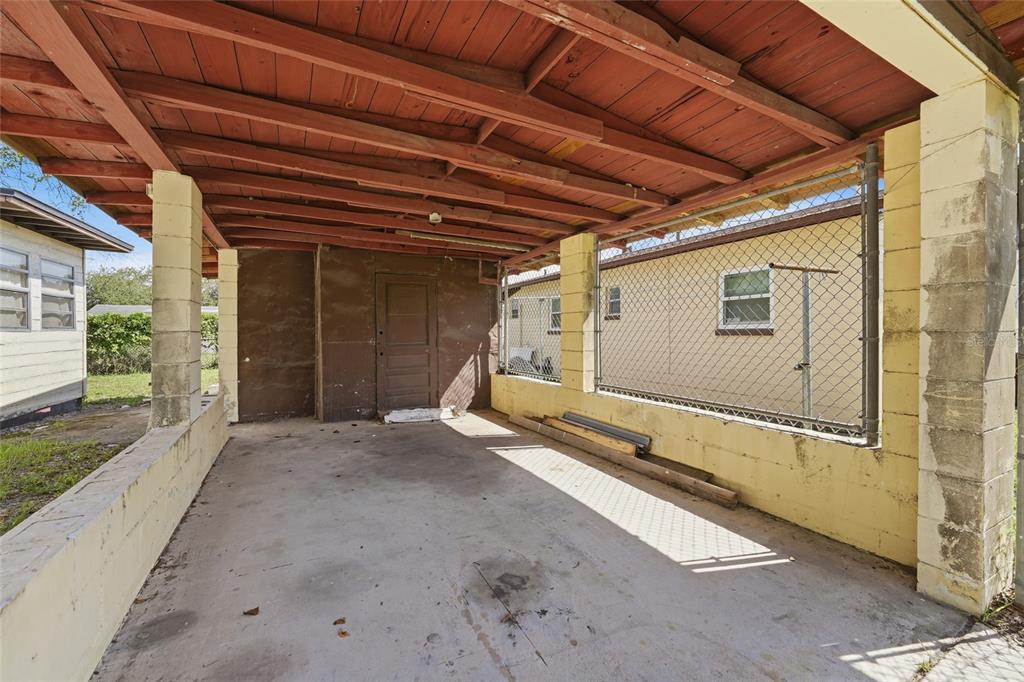 A covered concrete carport features a brown wooden door and yellow cinder block walls — 307 LEMON STREET, MAITLAND, FL