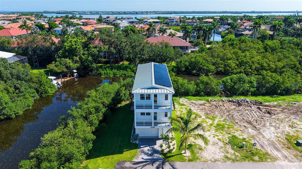 An aerial view shows a three-story house with solar panels situated beside a narrow canal — 12435 DOCKSIDE TERRACE, CORTEZ, FL