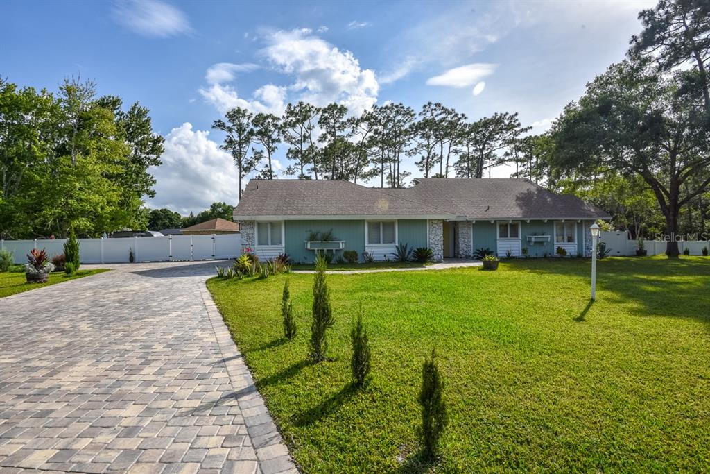 A single-story house with light green siding and a paver driveway sits on a lawn — 213 RIVERBEND ROAD, ORMOND BEACH, FL
