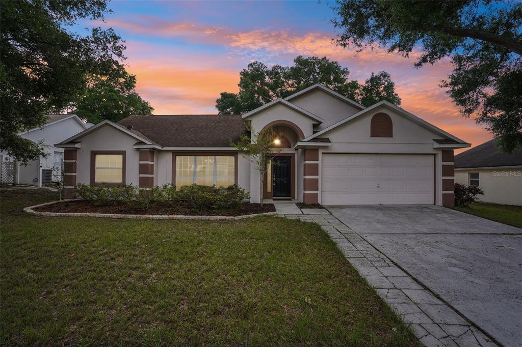 A single-story suburban house with a two-car garage, tan stucco exterior, and a paved driveway — 2596 ALCLOBE CIRCLE, OCOEE, FL