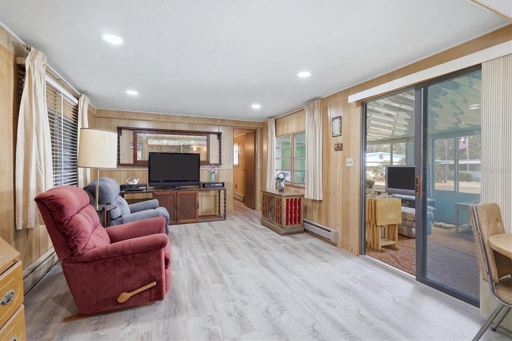 A living room features wood-paneled walls, light wood-look flooring, a red recliner, and sliding glass doors — 1112 46TH AVENUE DRIVE E, ELLENTON, FL