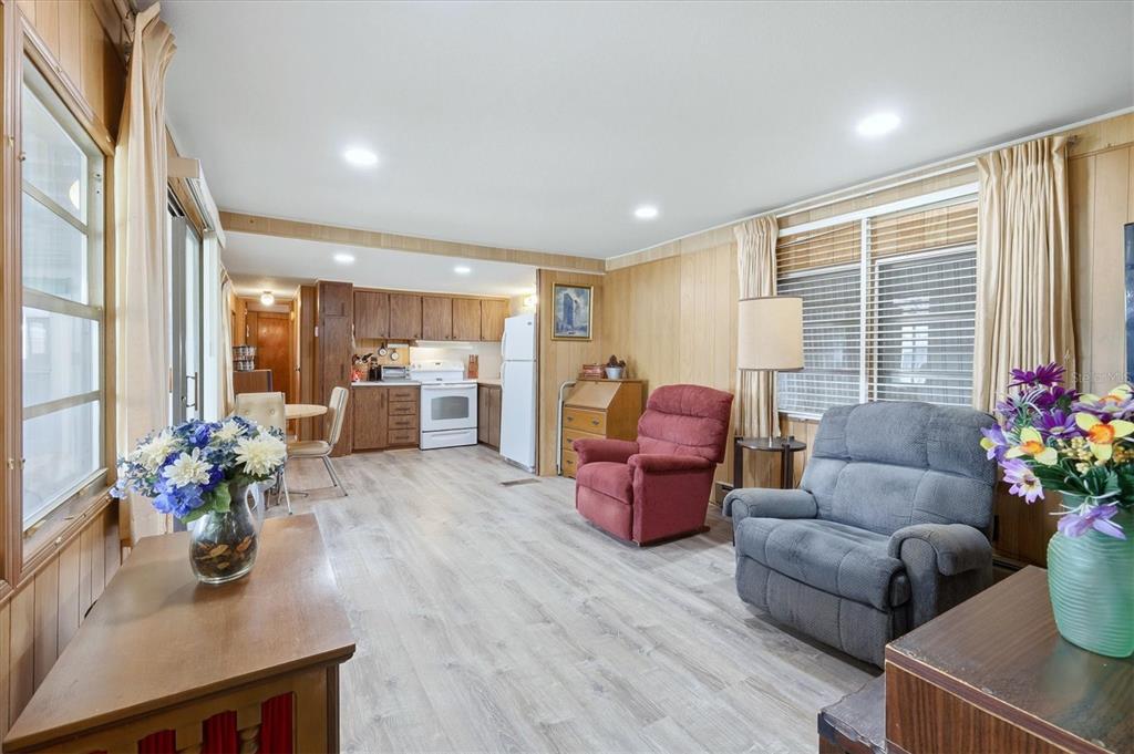 A living room with wood-paneled walls and light flooring flows into an open kitchen area — 1112 46TH AVENUE DRIVE E, ELLENTON, FL