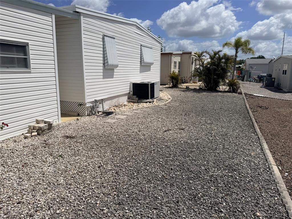 The exterior of a white mobile home features light-colored siding, window awnings, and a gravel yard — 3301 ALT 19 UNIT 267, DUNEDIN, FL