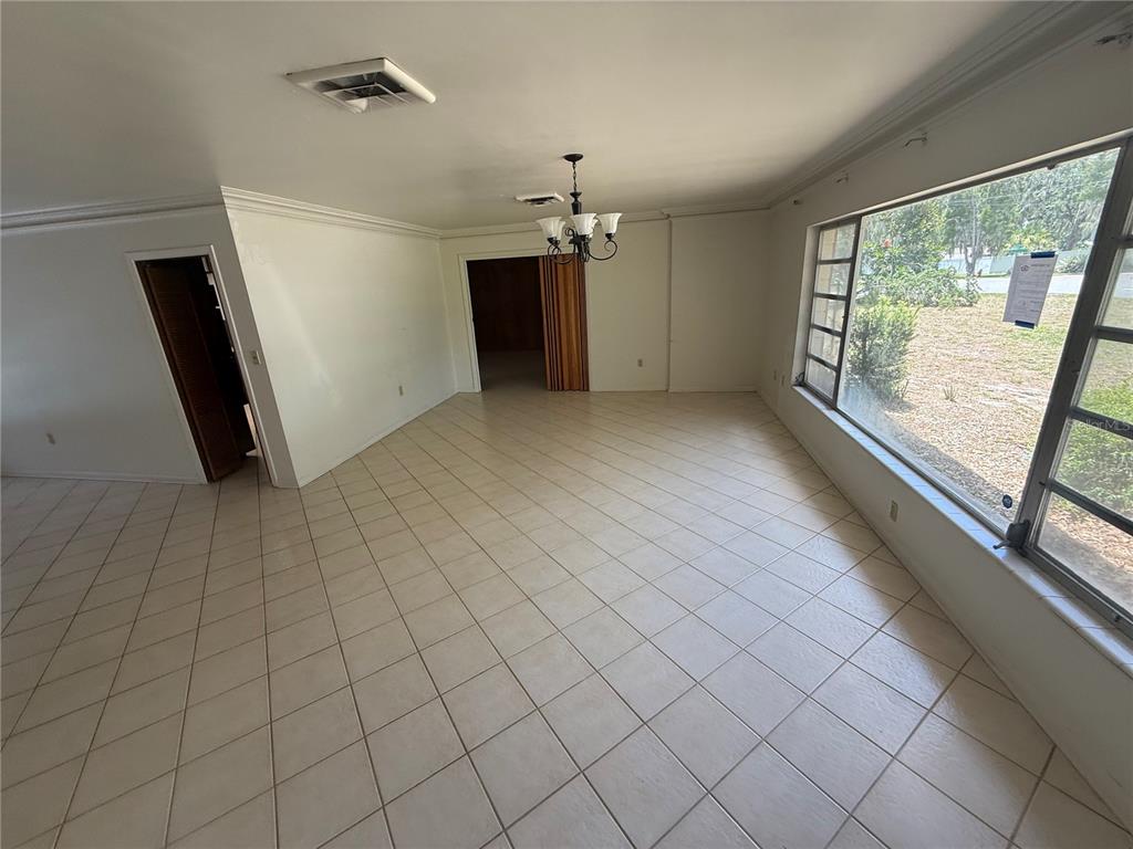 A bright living room features light-colored tile flooring, white walls, and a large window — 1015 E MANN ROAD, BARTOW, FL