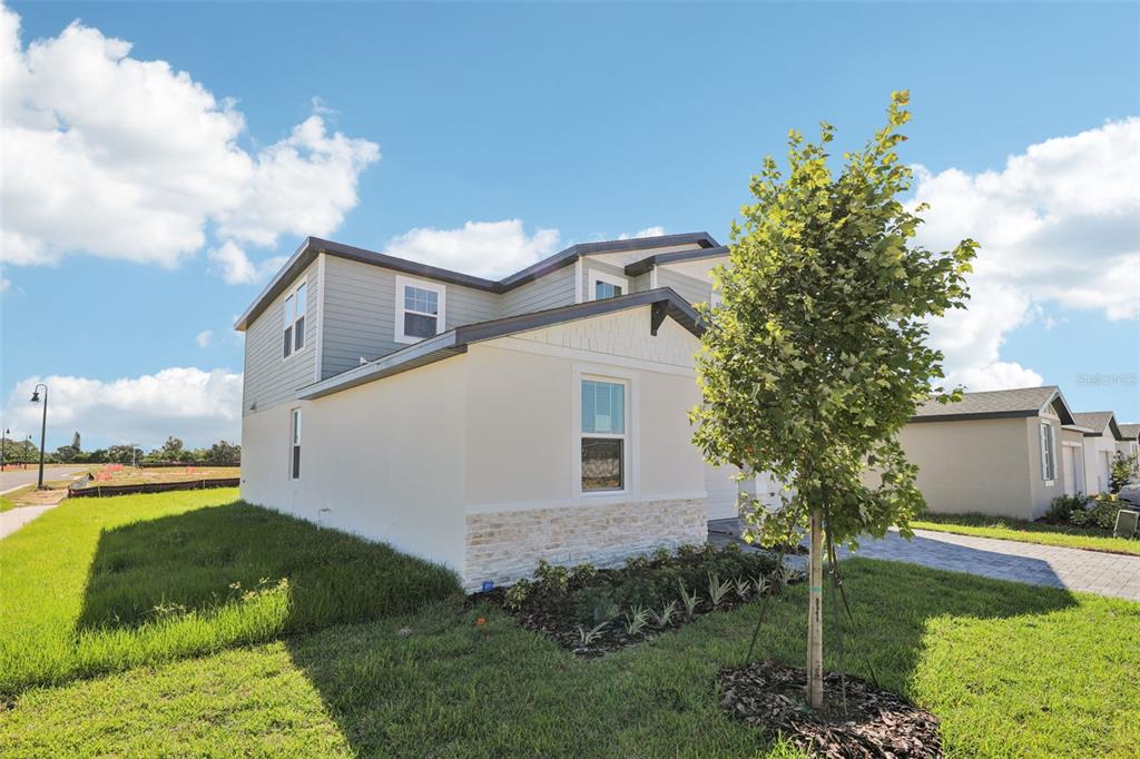 A two-story house with light-colored siding and stone accents sits on a grassy lot — 5222 GREEN BELT DRIVE, HAINES CITY, FL