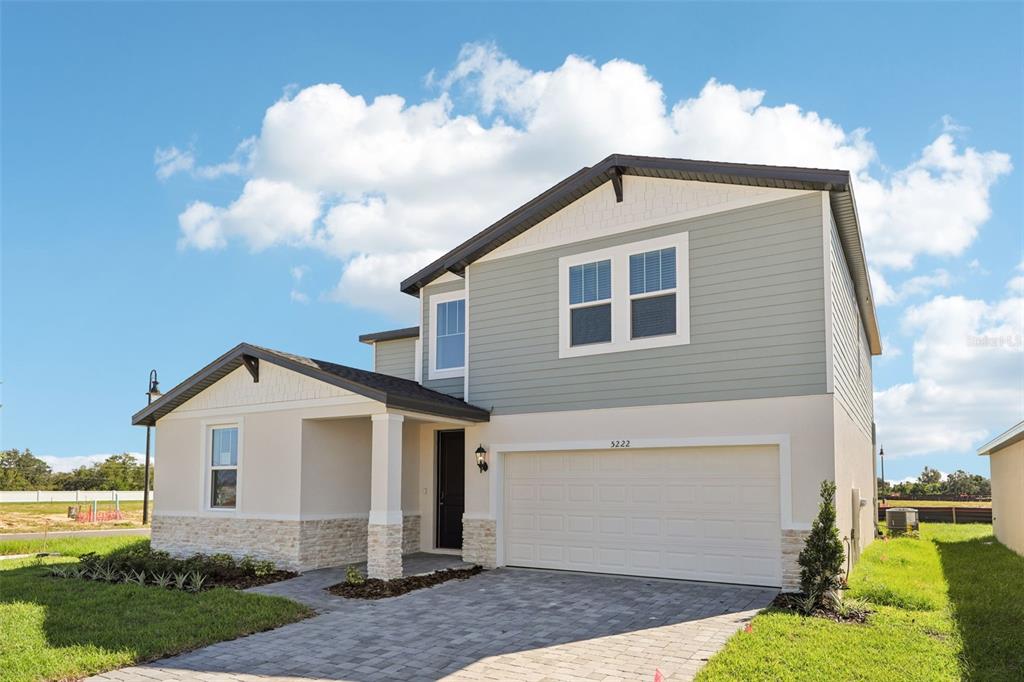 A two-story house with light-colored stucco, stone accents, and a paved driveway under a blue sky — 5222 GREEN BELT DRIVE, HAINES CITY, FL