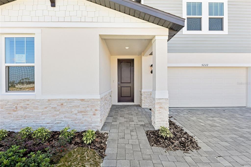 A front exterior view of a house featuring a stone-accented entryway and paved driveway — 5222 GREEN BELT DRIVE, HAINES CITY, FL