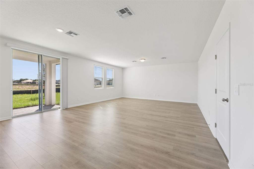 A spacious, empty living room with light wood-look flooring, white walls, and a sliding glass door — 5222 GREEN BELT DRIVE, HAINES CITY, FL