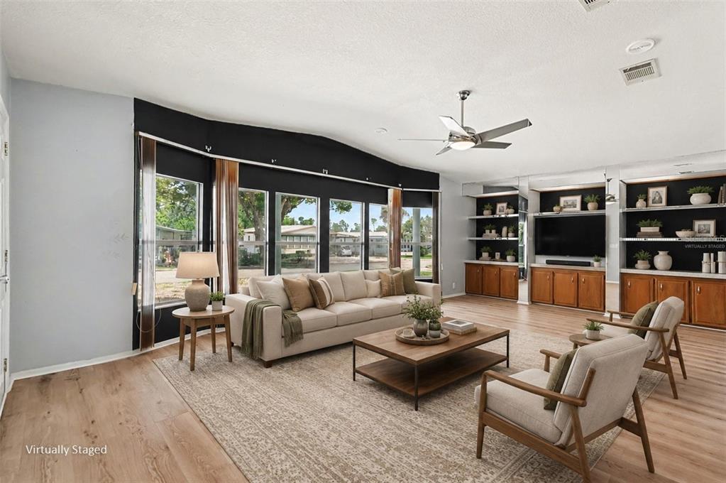 A virtually staged living room features a beige sofa, two armchairs, and built-in wooden shelving — 9178 ADMIRAL STREET, BROOKSVILLE, FL