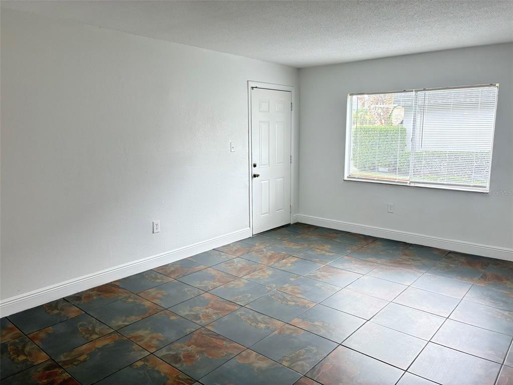 An empty room features white walls, a white door, a window with blinds, and tiled flooring — 1944 CONWAY ROAD UNIT 4, ORLANDO, FL