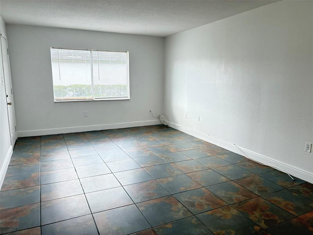 An empty room features white walls, a single window with blinds, and dark tiled flooring — 1944 CONWAY ROAD UNIT 4, ORLANDO, FL