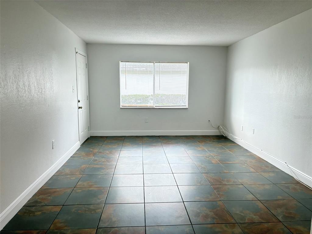 An empty room features white walls, a single window with blinds, and dark tiled flooring — 1944 CONWAY ROAD UNIT 4, ORLANDO, FL