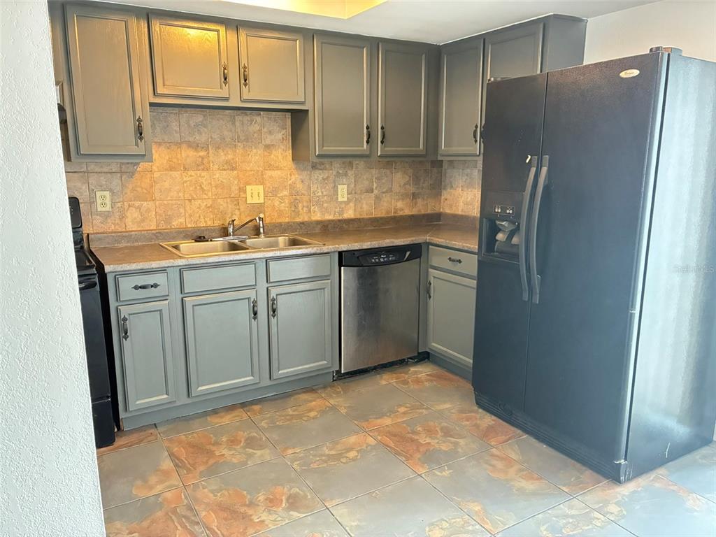 A kitchen features gray cabinets, stainless steel appliances, tiled backsplash, and mottled stone-look floor tiles — 1944 CONWAY ROAD UNIT 4, ORLANDO, FL