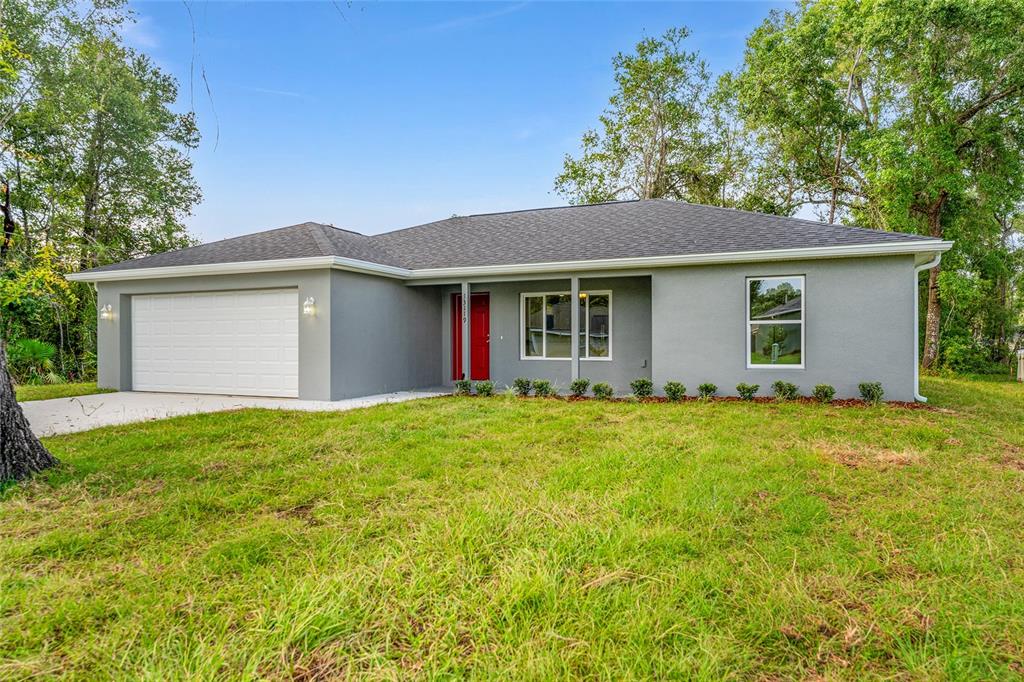 A single-story gray house with a white garage door and a bright red front door — 13119 NE 7TH LOOP, SILVER SPRINGS, FL