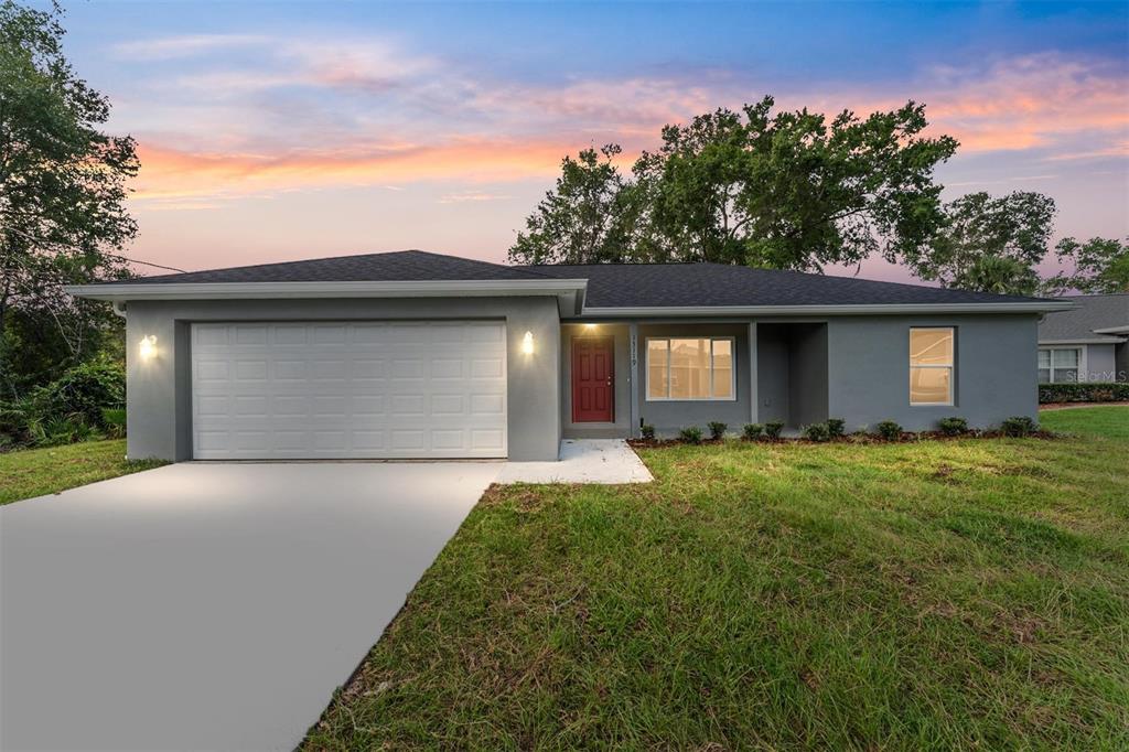 A gray single-story house with a two-car garage, red front door, and a concrete driveway — 13119 NE 7TH LOOP, SILVER SPRINGS, FL
