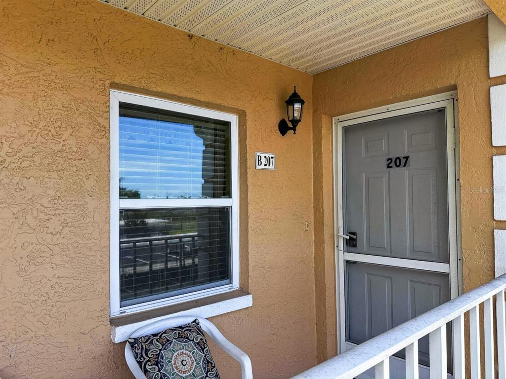 The exterior view shows a tan stucco wall with a window, a door labeled 207, and a light fixture — 1950 W CROWN POINTE BOULEVARD UNIT B207, NAPLES, FL