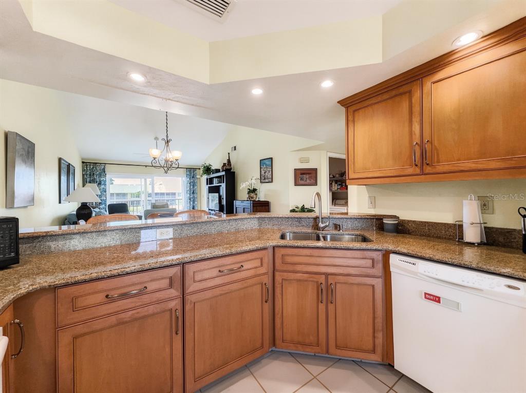 A kitchen features wood cabinets, granite countertops, a double sink, and a white dishwasher — 1950 W CROWN POINTE BOULEVARD UNIT B207, NAPLES, FL