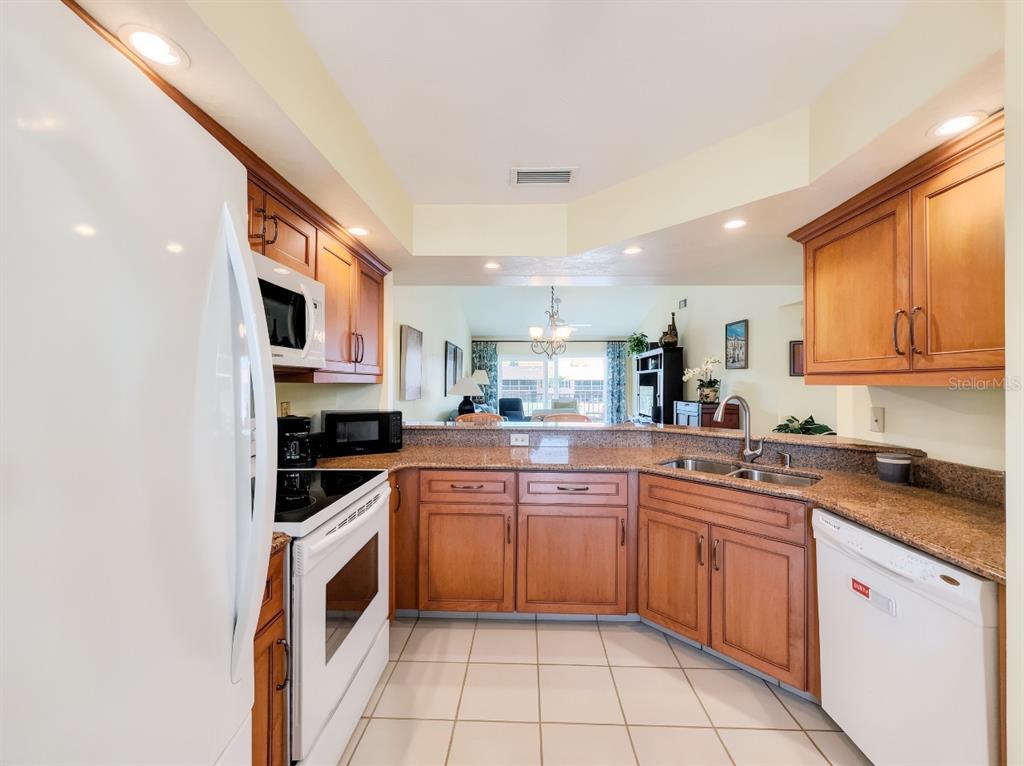 A kitchen with wood cabinets, granite countertops, white appliances, and tile flooring — 1950 W CROWN POINTE BOULEVARD UNIT B207, NAPLES, FL
