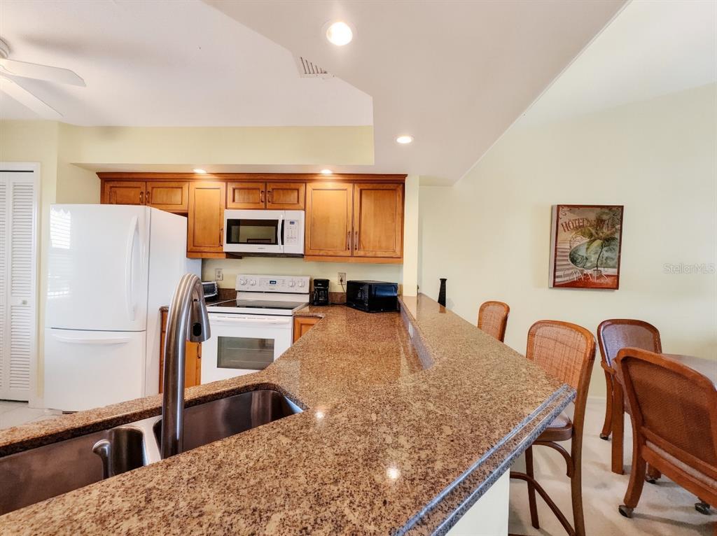 A kitchen features granite countertops, wood cabinets, a white refrigerator, and a breakfast bar — 1950 W CROWN POINTE BOULEVARD UNIT B207, NAPLES, FL