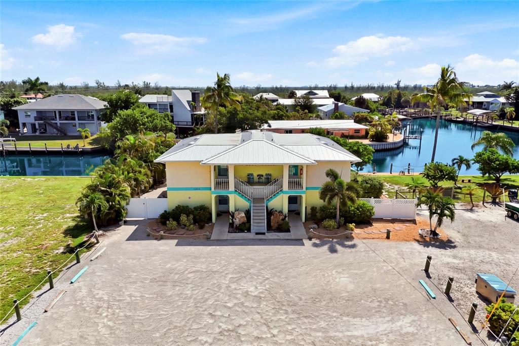 An elevated two-story building with a metal roof sits beside a canal and parking area — 3226 STRINGFELLOW ROAD, ST JAMES CITY, FL