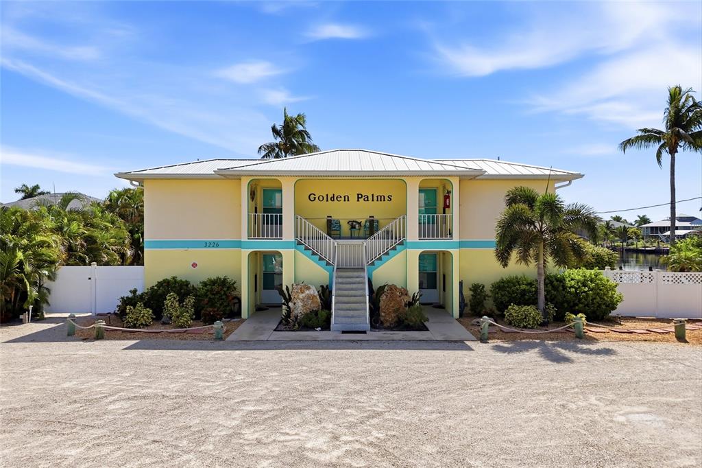 A two-story yellow building with a central staircase and palm trees under a blue sky — 3226 STRINGFELLOW ROAD, ST JAMES CITY, FL