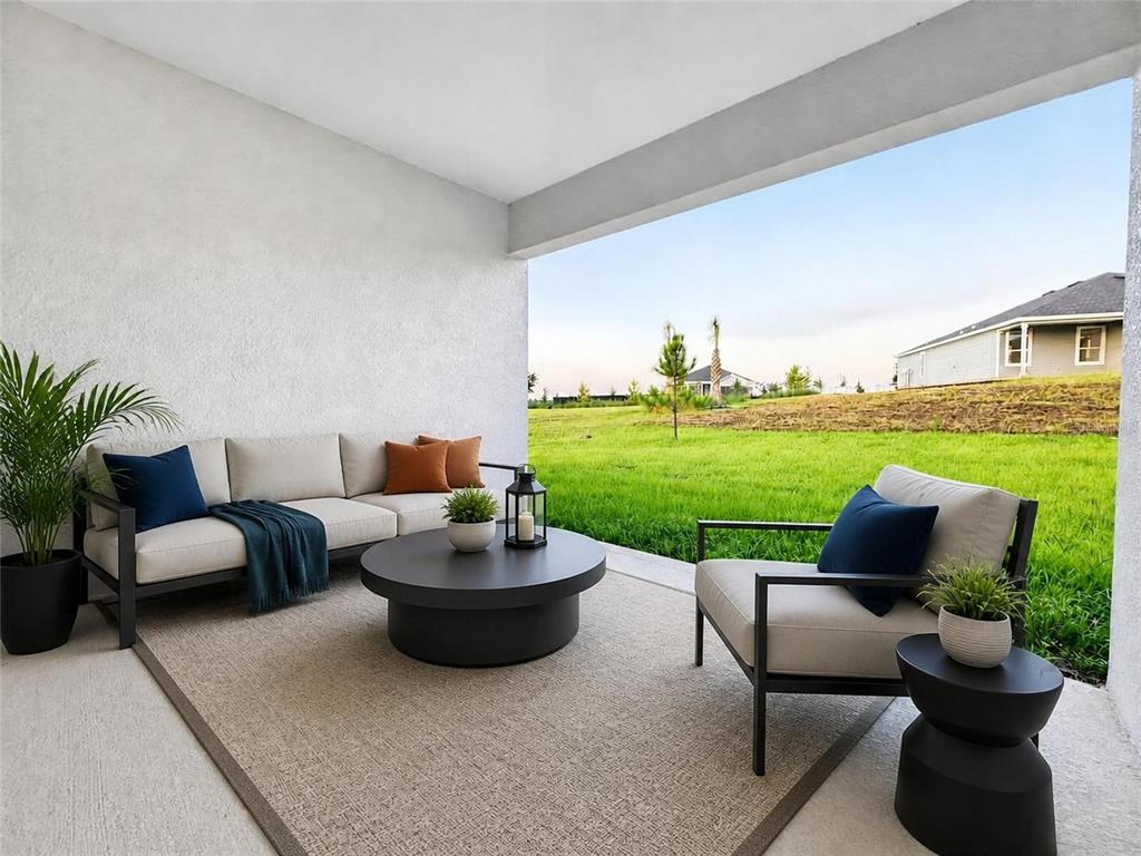 A covered patio features modern outdoor furniture, a round coffee table, and a grassy backyard — 187 PUMA LOOP, GROVELAND, FL