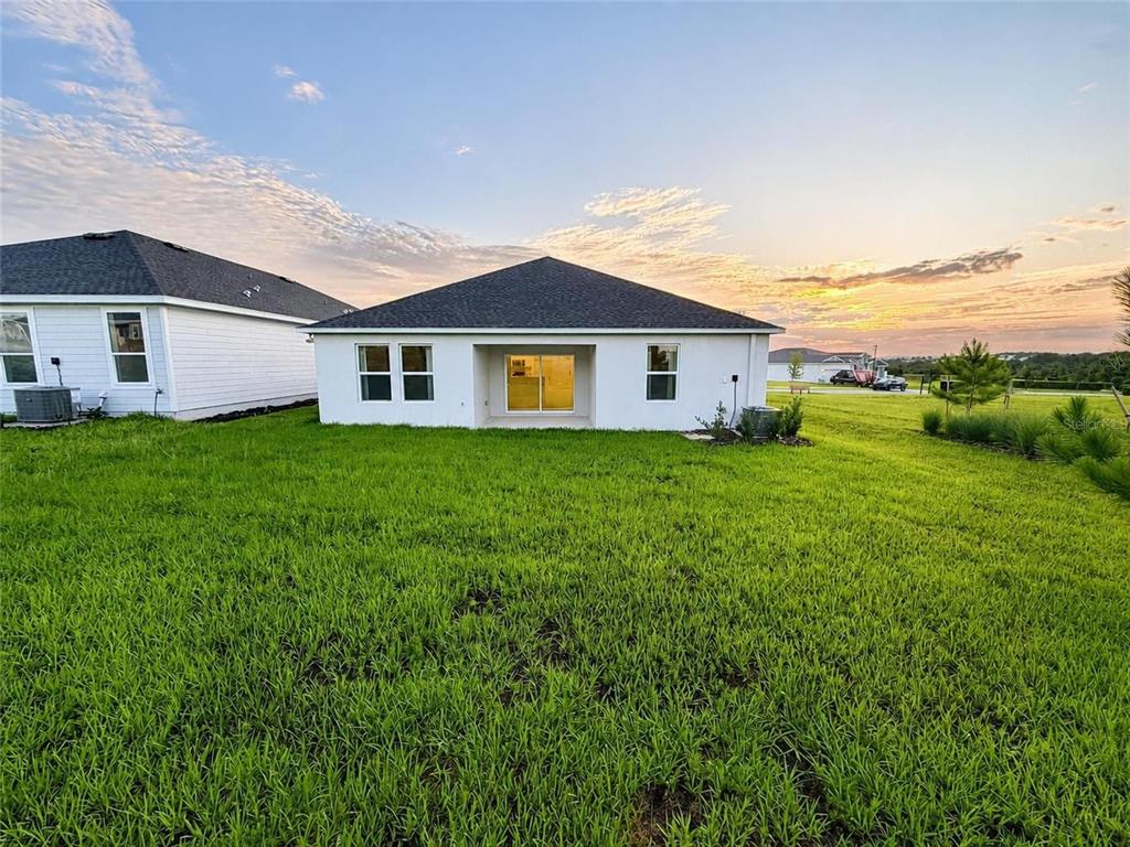 The rear exterior of a white single-story house with a large grassy yard — 187 PUMA LOOP, GROVELAND, FL