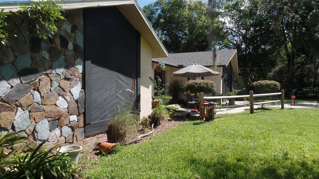 A house exterior features a stone wall, dark chevron-patterned siding, and a patio with furniture — 8057 DELAWARE DRIVE, WEEKI WACHEE, FL