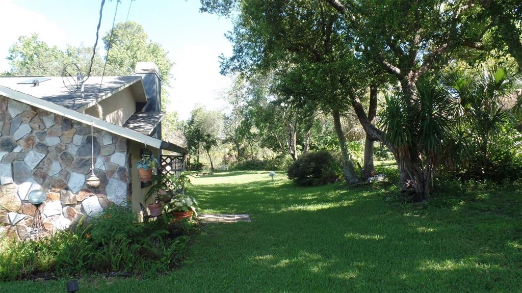 A stone-sided house exterior features a grassy backyard with large trees and landscaping — 8057 DELAWARE DRIVE, WEEKI WACHEE, FL