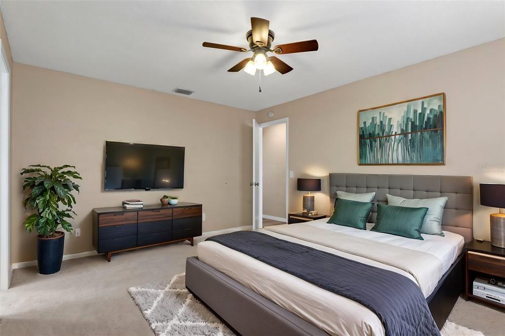 A bedroom features a gray upholstered bed, a dark wood dresser, a television, and a ceiling fan — 1628 BAKER ROAD, LUTZ, FL