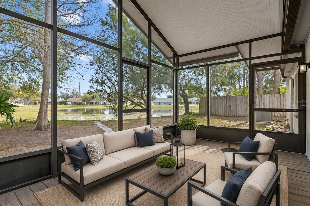 A screened-in porch with outdoor furniture overlooks a lake and a grassy backyard — 1628 BAKER ROAD, LUTZ, FL
