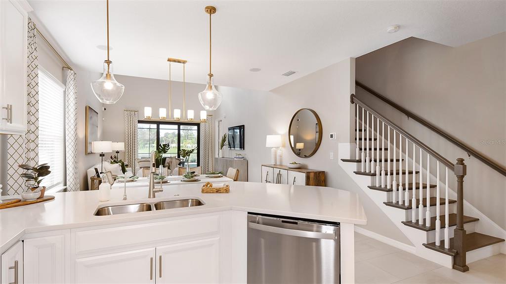 A kitchen with white cabinets and a stainless steel dishwasher overlooks a dining area — 32468 SEA LOCH LOOP, MOUNT DORA, FL