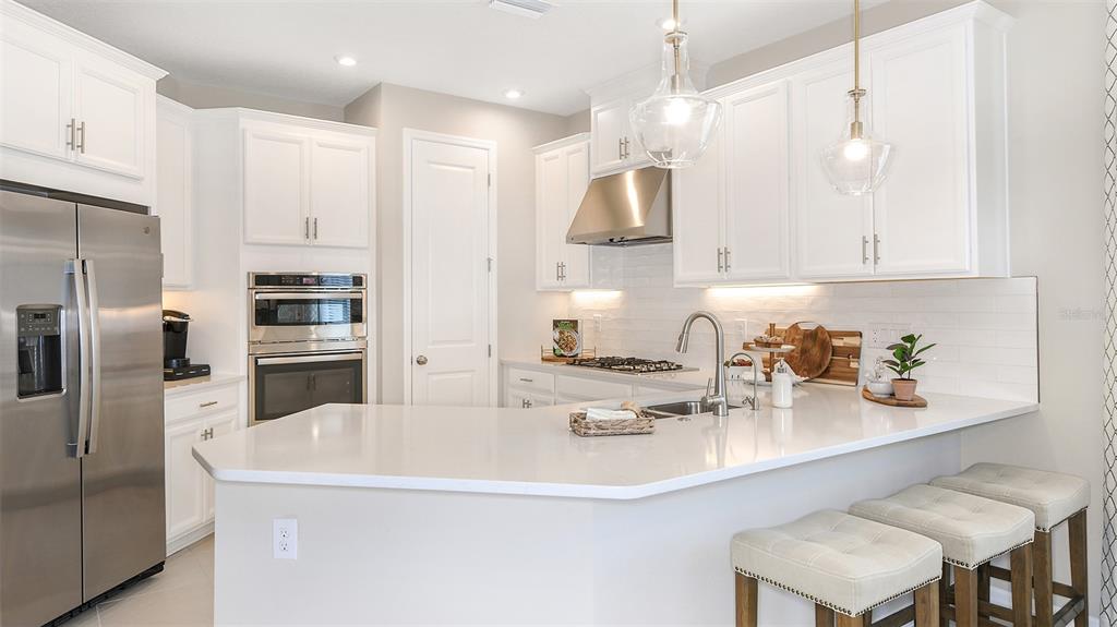 A modern kitchen features white cabinets, stainless steel appliances, a quartz island, and three stools — 32468 SEA LOCH LOOP, MOUNT DORA, FL