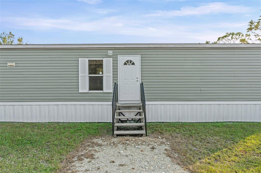 The exterior of a light green manufactured home features a single door with stairs — 8414 SWEDEN BOULEVARD, PUNTA GORDA, FL