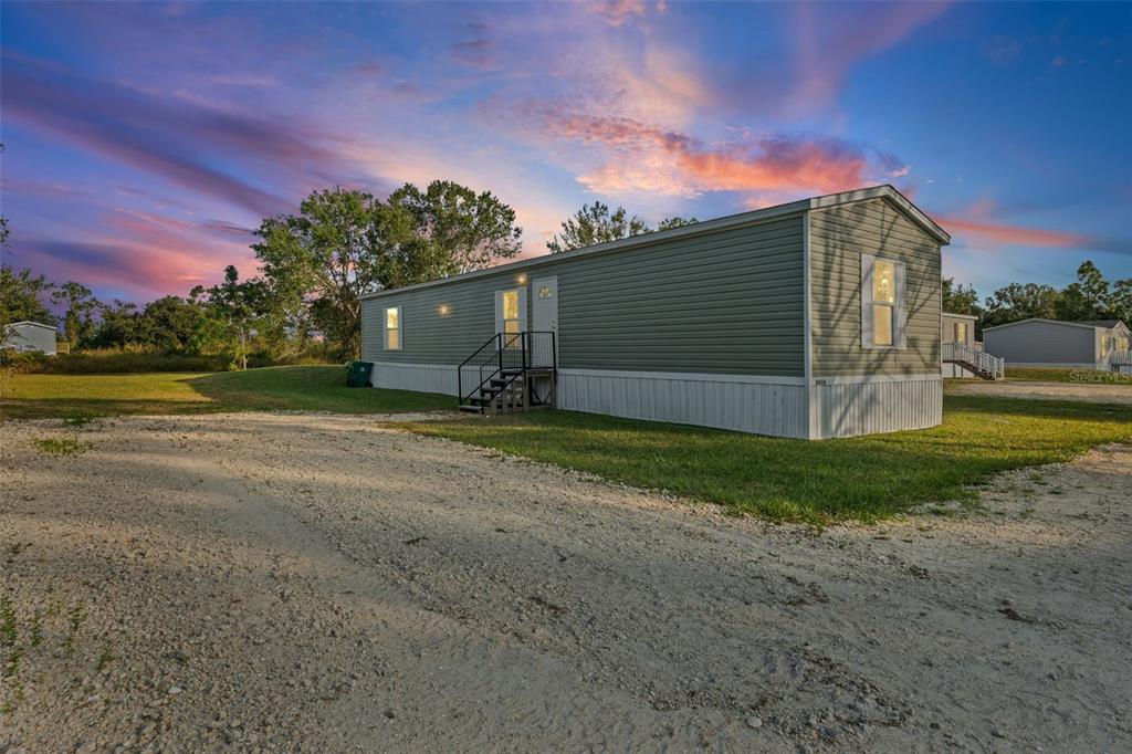 A single-story manufactured home with light green siding sits on a gravel lot at sunset — 8414 SWEDEN BOULEVARD, PUNTA GORDA, FL