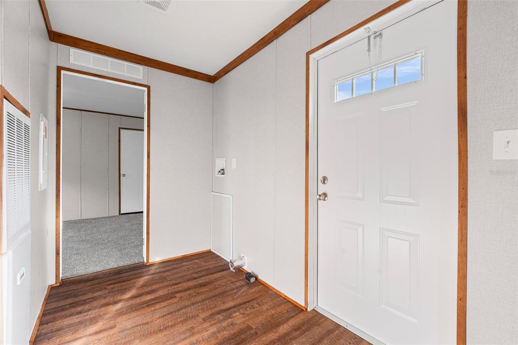 A utility room with wood-look flooring, a white exterior door, and a doorway to a bedroom — 8414 SWEDEN BOULEVARD, PUNTA GORDA, FL