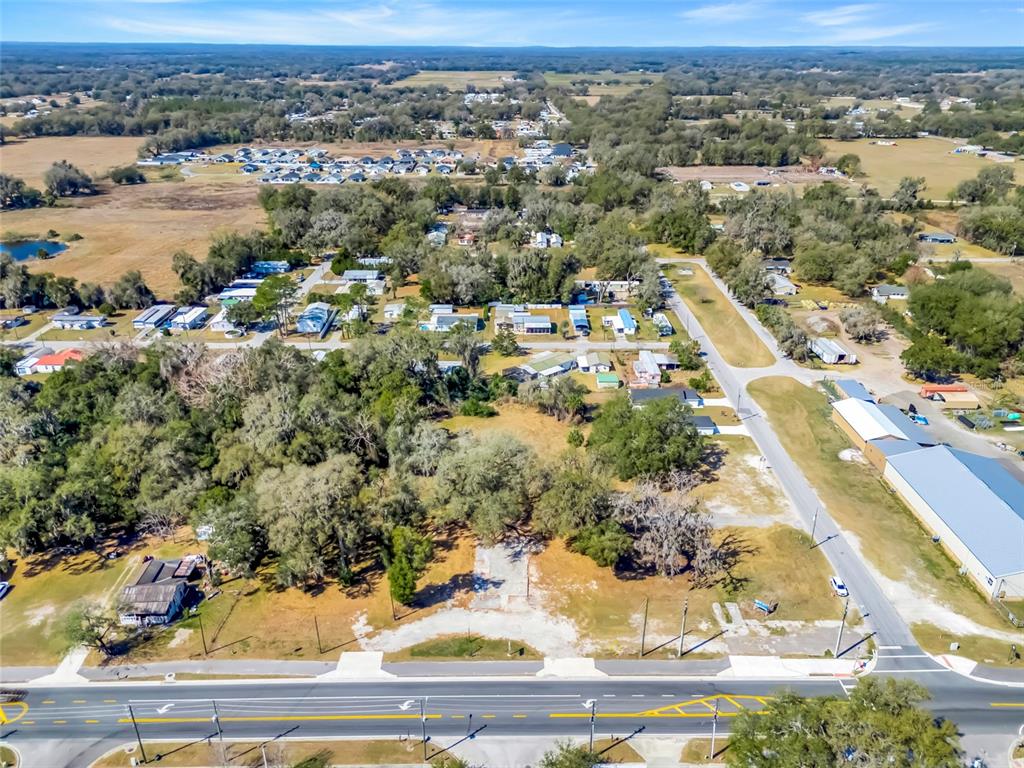 An aerial view shows a vacant corner lot with mature trees near a paved road — 82 S MARKET BOULEVARD, WEBSTER, FL